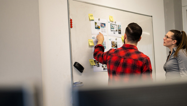 Man wijst naar uitgeprinte webpagina's op een whiteboard terwijl een collega meekijkt
