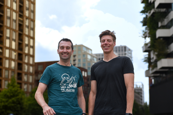 Twee lachende mannen in T-shirt staan buiten tussen moderne hoge gebouwen