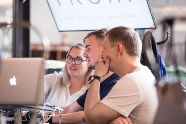 Drie collega's kijken samen naar een laptop en overleggen aan een werktafel