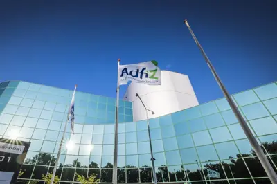 Glazen kantoorgebouw met een vlag met het Adfiz-logo tegen een strakblauwe lucht