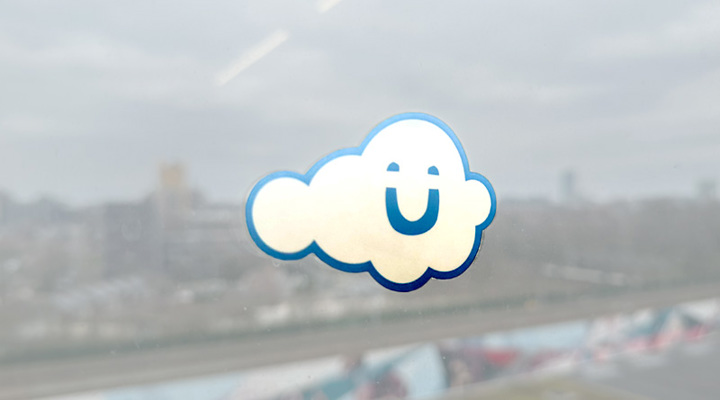 Sticker van een lachend wolkje met het Umbraco-logo op een raam met uitzicht over de stad