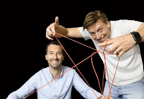 Twee lachende mannen spannen samen een web van oranje touw voor een zwarte achtergrond