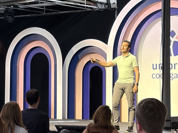 Spreker geeft een presentatie op een podium met gekleurde bogen en een deels zichtbaar Umbraco-logo