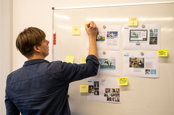 Man schrijft op een whiteboard met uitgeprinte websiteontwerpen en gele memobriefjes
