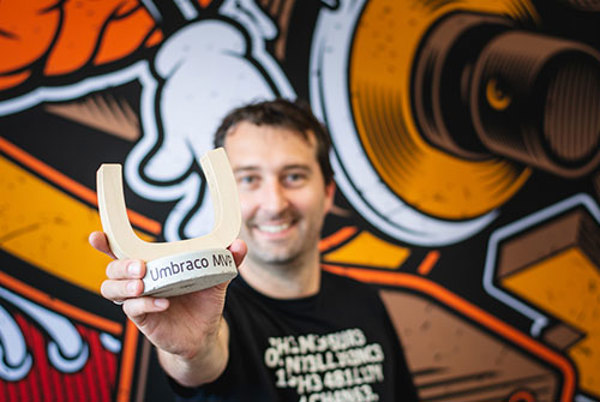 Lachende man toont een Umbraco MVP-award voor een kleurrijke muurschildering