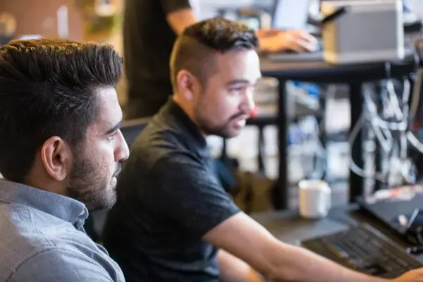 Twee mannen kijken geconcentreerd naar een scherm aan een werkplek vol computerapparatuur